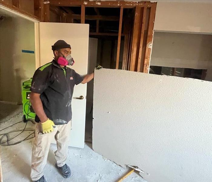 technician in gloves and mask holding a piece of sheetrock